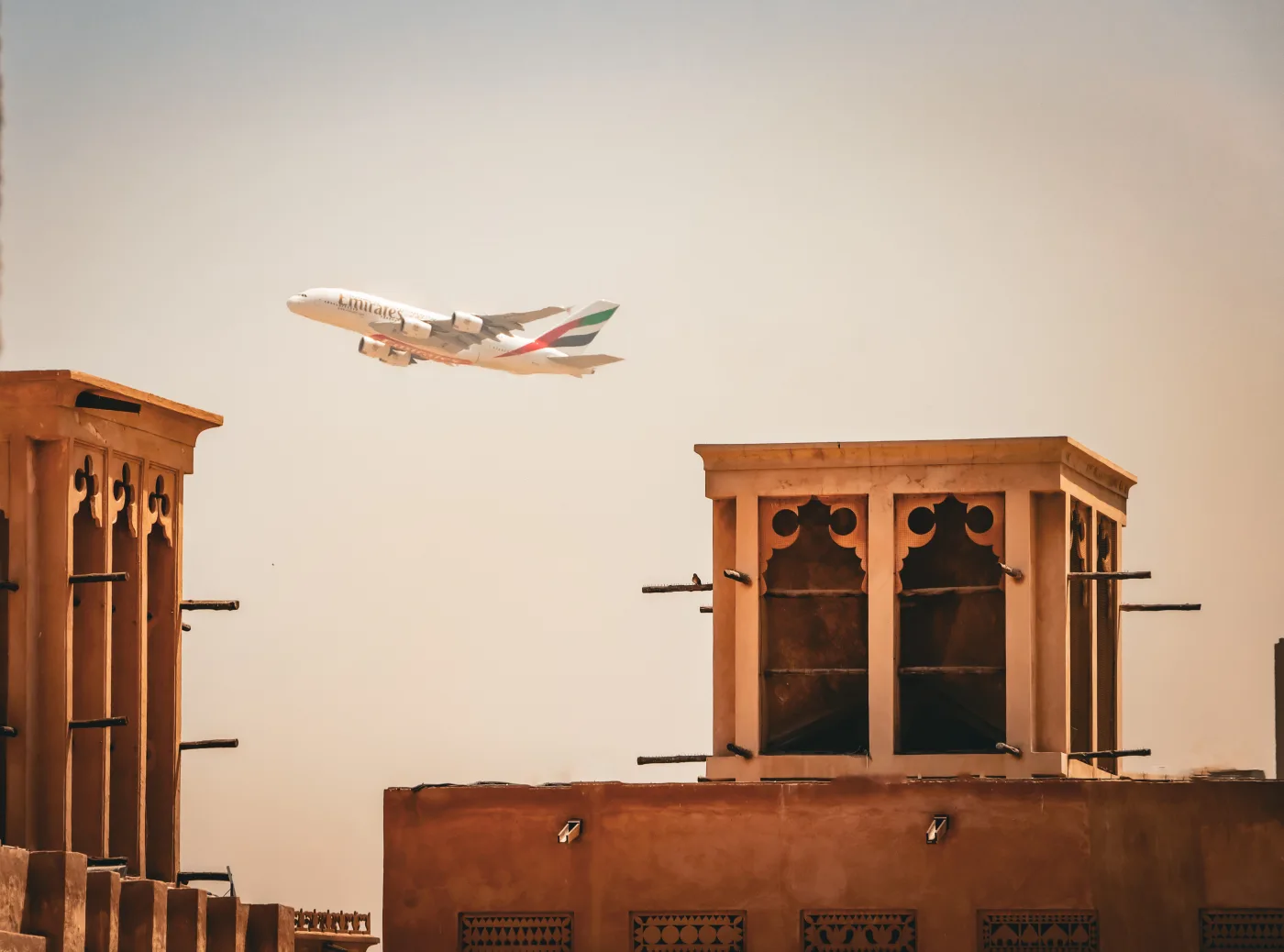 Traditional wind-tower architecture in Dubai's Al Fahidi historic district, with an aircraft passing overhead